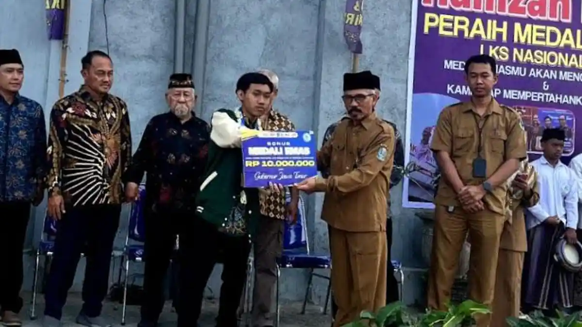 Siswa SMK peraih juara nasional lomba welding berpose memegang medali emas di ruang praktik sekolah dengan latar belakang peralatan las.